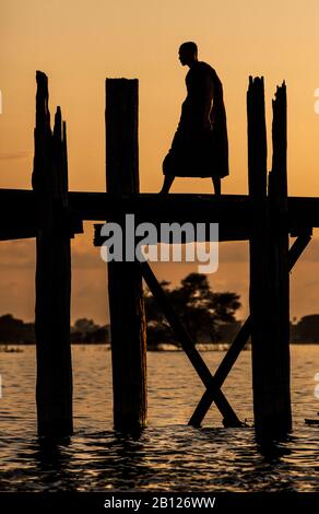 Buddhistischer Mönch, der bei Sonnenuntergang über U Beins Brücke spazieren ging. Amarapura, Myanmar Stockfoto