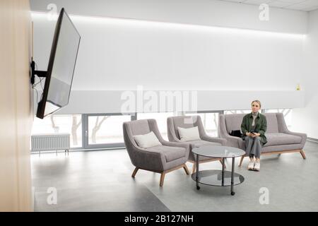 Junge Casual Woman, die auf der Couch im modernen medizinischen Zentrum sitzt Stockfoto