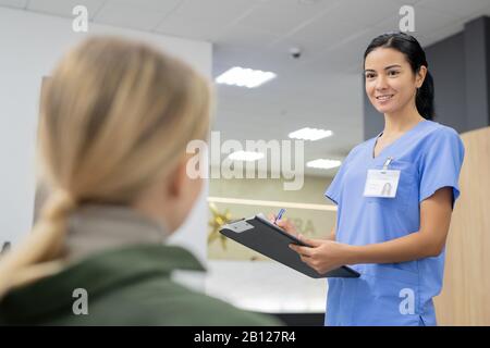 Ziemlich junger Brunette-Assistent in blauer Uniform, der einen der Patienten betrachtet Stockfoto