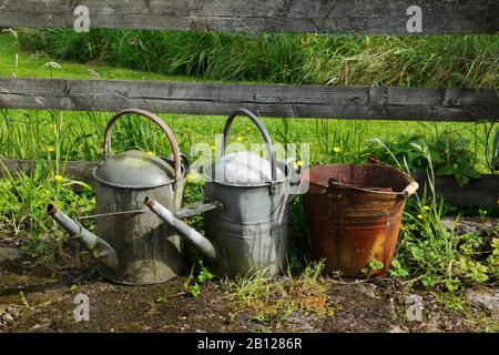 Zwei glanzverglitzerte Gießkannen und ein rostiger verzinkter Eimer, mit dem Asche von einem Kohleflöz gesammelt wurde. Zeigt die Wirkung von saurem Wasser auf Metall an. Stockfoto