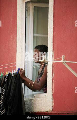 Eine schwarze Dame erreicht das Fenster und hängt Wäsche an der Außenwand des Hauses Stockfoto
