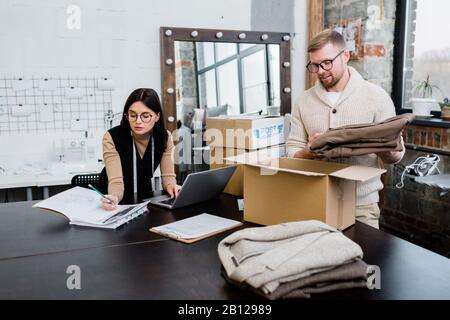 Junger Mann, der die Hose in die Kartonverpackung legt, während er das Paket für den Kunden verpackt Stockfoto