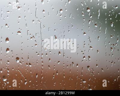 Regen fällt auf die Fensteroberfläche mit trübem Hintergrund . Natürliches Muster von Regentropfen isoliert auf verschwommenem Hintergrund. Stockfoto