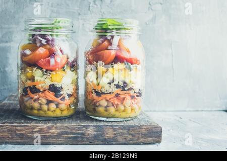 Köstlicher frischer vegetarischer bunter Salat in den Gläsern mit Kichererbsen, Paprika, Gurke, Karotte, getrockneten Preiselbeeren, Tomaten, roter Zwiebel und Kürbisse Stockfoto