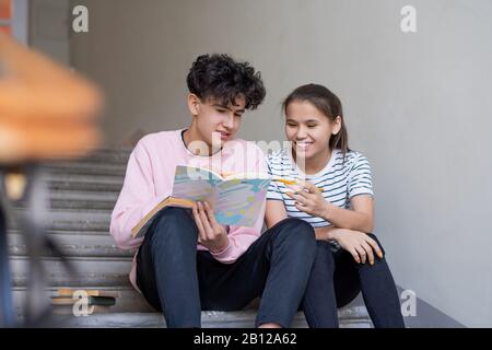 Clever Junge und Mädchen, die auf Seite des Nachahmerbuchs zeigen, während sie die Vortragsnotizen diskutieren Stockfoto