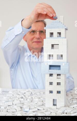 Reifer Architekt, der ein Haus aus Spielzeugblöcken errichtet Stockfoto