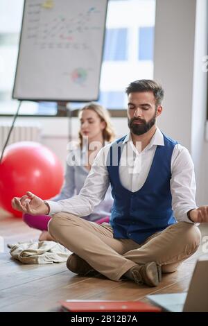 Geschäftskollegen meditieren bei der Arbeit, sitzen auf dem Boden im modernen Büro. Modern, Business, Meditation, Visualisierung, Entspannung, Konzept Stockfoto