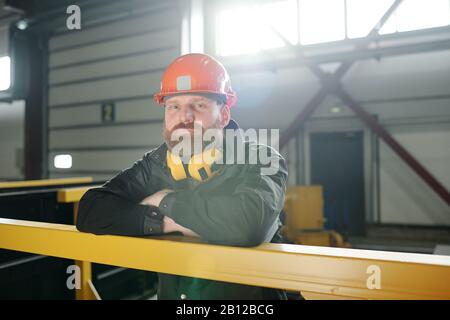 Junger bärtiger Mann in schützender Arbeitskleidung, der an der gelben Stange steht Stockfoto
