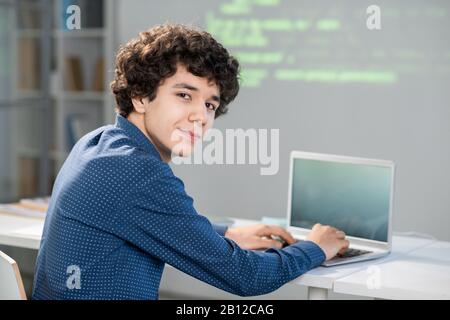 Cleverer Student mit lockigen Haaren, der Sie bei der Arbeit mit technischen Daten betrachtet Stockfoto