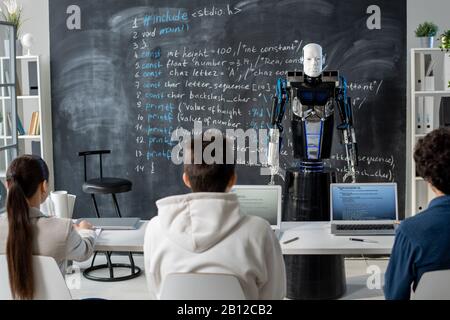 Rückansicht der Reihe von Studenten, die am Schreibtisch vor dem Automationsroboter sitzen Stockfoto