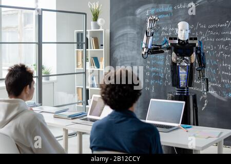 Zwei männliche Studenten, die sich mit einem Automationsrechnerroboter auf der Tafel befinden Stockfoto