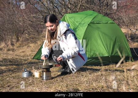 Fröhliche Frau, die allein vor ihrem Zelt kochte Stockfoto