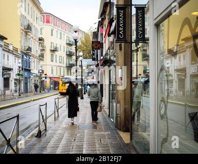 Nice, Frankreich - 24. November 2019: Ruhiges Viertel im Zentrum von Nizza mit Fußgängern, die an einem regnerischen Tag mit Sonnenschirmen auf einer Einkaufsstraße laufen Stockfoto