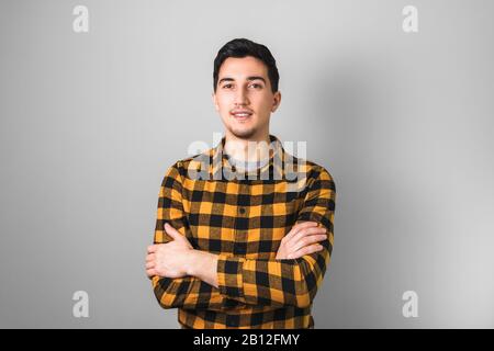 Hübsch aussehender Kerl in gelbem, quadratischem Hemd mit auf grauem Hintergrund gekreuzten Armen Stockfoto