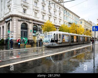 Nizza, Frankreich - 24. November 2019: Traditionelle Straßenbahn Nizza an einem regnerischen Tag mit Fußgängern, die auf der Avenue Jean Medecin und der Bank BNP Paribas im Hintergrund laufen Stockfoto