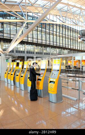 Automated Check-in Terminals von Lufthansa und einem jungen, selbstbewussten Geschäftsmann, der einen Anzug und ein Gepäck für eine Geschäftsreise am Flughafen Hamburg, Hamburg, Deutschland, Europa trägt Stockfoto