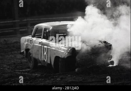 1970er Jahre, historisch, Stock-Car-Rennen, Harringay Stadium, London, England, zeigt ein beschädigtes "banger" Auto mit Rauch, das von seinem beschädigten Motor kommt, nachdem er von einem anderen Konkurrenzauto getroffen wurde, was im "banger Racing" erlaubt ist. Stockfoto