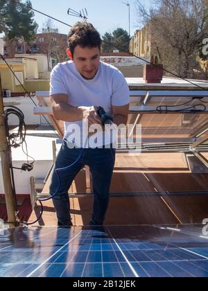 Kaukasisch attraktiver junger Mann, der Solarpaneele mit einem Schlauch säubert. Alternative Stromquelle, nachhaltige Ressourcenkonzeption. Stockfoto