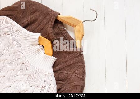 Zwei Strickpullover für Damen und Herren auf Holzhängern auf weißem Holzhintergrund mit flacher Draufsicht Stockfoto