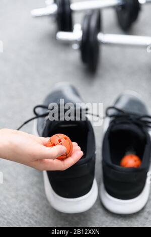 Hand, die einen frischeren Ball über Trainingsschuhe mit Hanteln im Hintergrund hält. Konzept zur Vermeidung von unangenehmem Geruch im Schuhwerk Stockfoto
