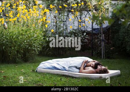 Liebendes Paar liest schlafend auf einer Matratze im Garten Stockfoto