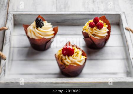 Muffins mit belgischer Schokolade und weißer Schokoladencreme und Mascarpon mit Beeren auf einem Holztablett Stockfoto