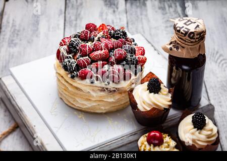 Pfannkuchen mit einer Kappe aus Beeren, die in weißer Schokolade auf einem weißen Holztisch mit ein paar belgischen Muffins und einer Flasche Sirup gezaucht ist Stockfoto