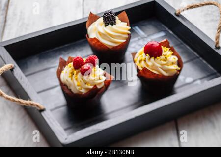 Muffins mit belgischer Schokolade und weißer Schokoladencreme und Mascarpon mit Beeren auf einem Holztablett Stockfoto