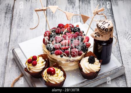 Pfannkuchen mit einer Kappe aus Beeren, die in weißer Schokolade auf einem weißen Holztisch mit ein paar belgischen Muffins und einer Flasche Sirup gezaucht ist Stockfoto