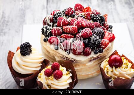 Pfannkuchen mit einer Kappe Beeren, die in weißer Schokolade auf einem weißen Holztisch mit ein paar belgischen Muffins gedrillt ist Stockfoto