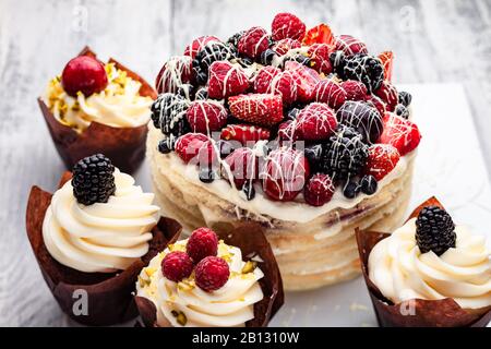 Pfannkuchen mit einer Kappe Beeren, die in weißer Schokolade auf einem weißen Holztisch mit ein paar belgischen Muffins gedrillt ist Stockfoto