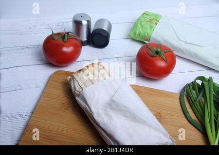 Zwei Doner-Kebabs, Zwiebel, Salzschüttler und Tomaten auf weißem Holzhintergrund lagen flach Stockfoto