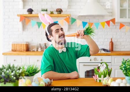 Frohe Ostern. Ein lustiger bärtiger Mann, der in einem dekorierten Zimmer Karotten isst. Stockfoto