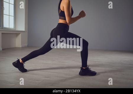 Squat-Übungen. Mädchen in schwarzer Sportkleidung mit Hanteln in den Händen, die in einem Raum hocken. Stockfoto