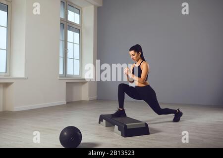 Squat-Übungen. Mädchen in schwarzer Sportkleidung mit Hanteln in den Händen, die in einem Raum hocken. Stockfoto