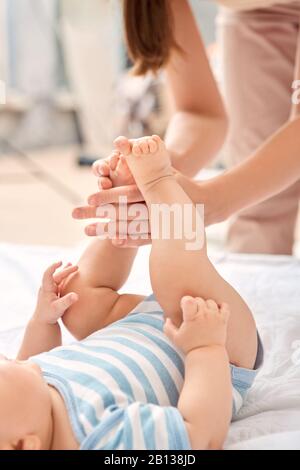 Junge Erwachsene Frau, die ihrem kleinen neugeborenen Baby eine sanfte Massage macht Stockfoto