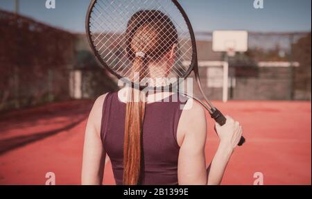 Schönes und schlankes Mädchen mit Schläger spielt Tennis, Mädchen steht mit dem Rücken zum Zuschauer Stockfoto