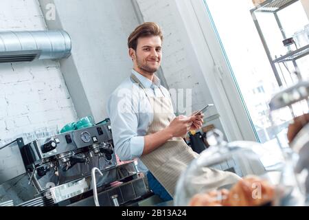 Junger, erwachsener Barista, der im Restaurant mit modernem Tablet arbeitet Stockfoto