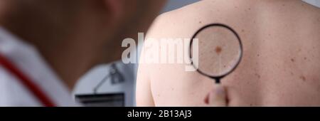 Männlicher Arzt Blick auf die Lupe auf der Haut des Patienten Stockfoto