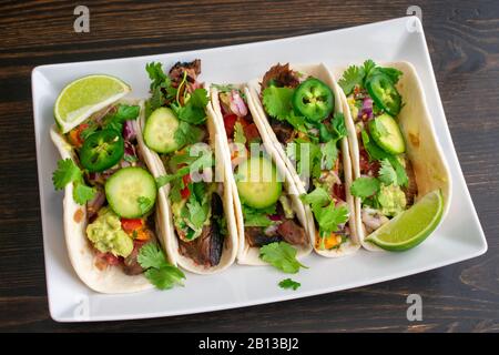 Gegrillte Flanke Steak Tacos mit Guacamole und Pico de Gallo: Platte aus Rindfleisch Tacos in Mehltortillas mit Cilantro, Gurke und jalapeños Stockfoto