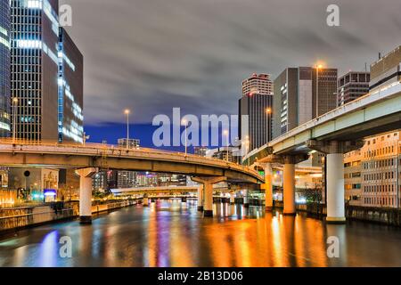 Autobahnbrücken, die bei Sonnenaufgang zwischen hoch aufragenden Bürstentürmen über den Stadtbogen von Osaka führen. Stockfoto