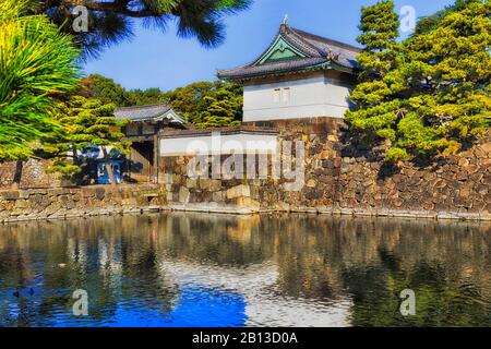 Weiße historische Türme an Steinmauern rund um den kaiserlichen Palast in der Stadt Tokio, umgeben von Wassergraben an einem sonnigen Tag. Stockfoto