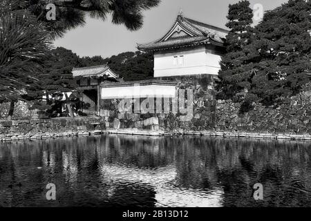 Schwarz-weiße historische Türme an Steinmauern rund um den kaiserlichen Palast in der Stadt Tokio. Spiegelung im wassergefüllten Wassergraben. Stockfoto