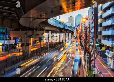 Gebogene Rampe einer Autobahn über Straßen in Osaka, der Stadt Japan, bei Sonnenaufgang mit Beleuchtung und passender Straßenfahrt. Stockfoto