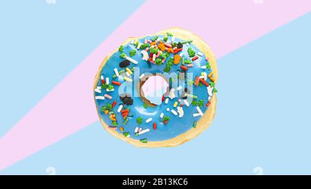 Levittierende blaue Krapfen mit bunten Einstreuen auf blauem und rosafarbenem Baumwoll-Kerzenhintergrund. Dessert buntes Pop-Art-Essen in den Farben der 80er Jahre im Retro Stockfoto