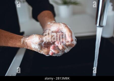 Nahaufnahme der Hände des Menschen in Seifenschaum. Finger und Handflächen waschen und reinigen. Wasser, das aus dem Hahn in das Waschbecken in der Küche strömt. Handpflege und Protec Stockfoto