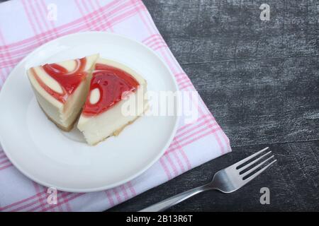 Zwei Käsekuchen auf einem Teller auf rot-weißer Serviette auf schwarzem Holzhintergrund lagen flach. Bild enthält Kopierbereich Stockfoto