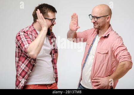 Zwei freundlich lächelnde Männer grüßen sich und geben hohe fünf. Stockfoto