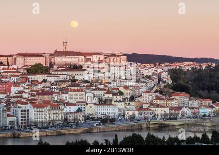 Mondaufgang und Sonnenuntergang über Coimbra in Portugal. Blick auf die alten Häuser, den University Tower, den Largo da Portagem und den Fluss Mondego. Stockfoto