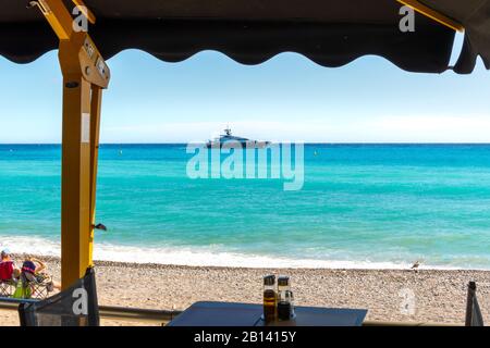 Blick auf eine Yacht im Mittelmeer von einem Café am Meer in Menton, Frankreich, als Lounges am Strand. Stockfoto
